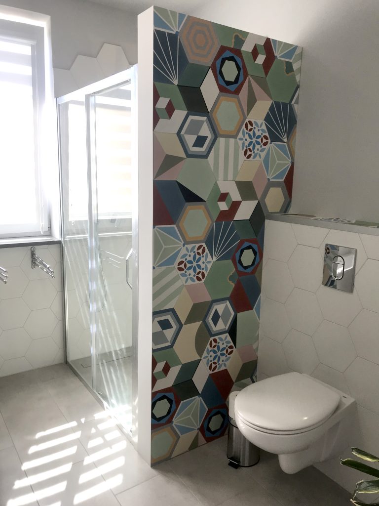 Kolorowa ściana w łazience przy toalecie zrobiona z sześciokątnych płytek cementowych