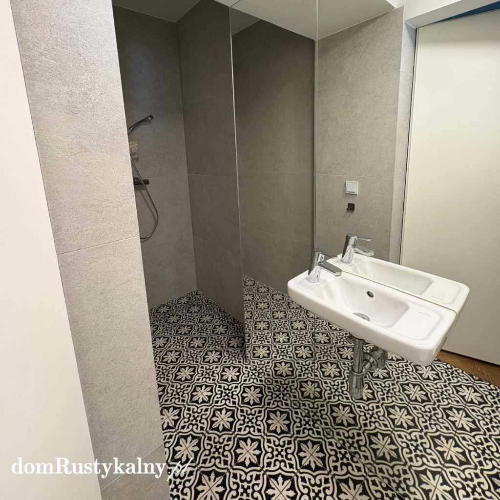 Wąska łazienka z lustrzaną szafką i podłogą z płytek cementowych w czarno‑biały wzór – jaki kolor wybrać do małej łazienki, geometria, duże lustro